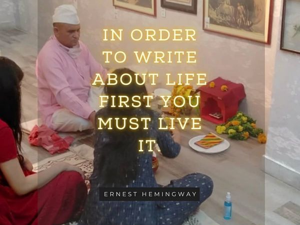 People sitting on the floor in a room with framed pictures and a quote by Ernest Hemingway.