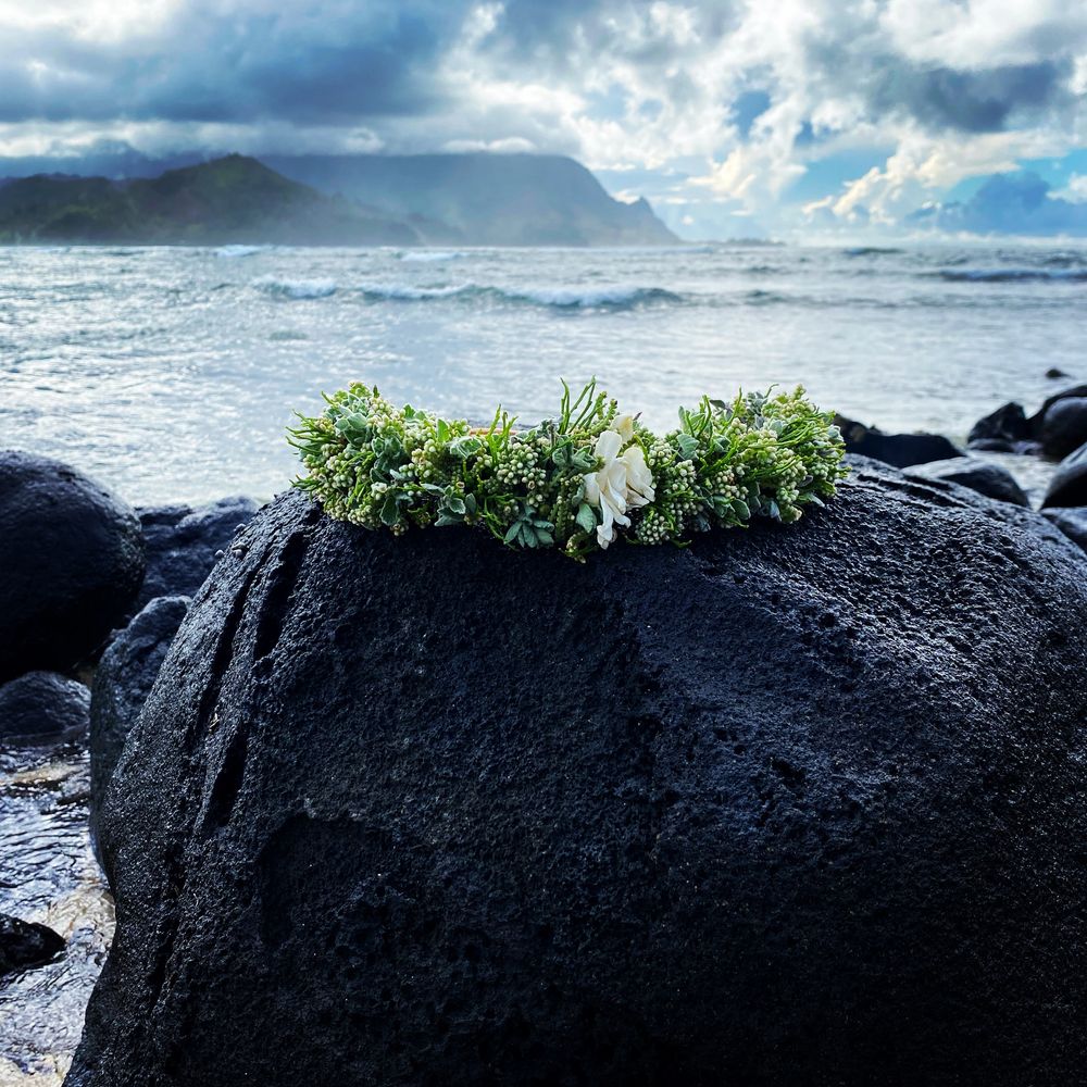 Hanalei, Kauai, a lei crowns a pohaku (black lava rock) in view of the Napali Coast and Makana Peak