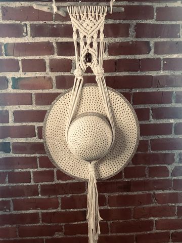 Crocheted hat holder hanging on a brick wall.