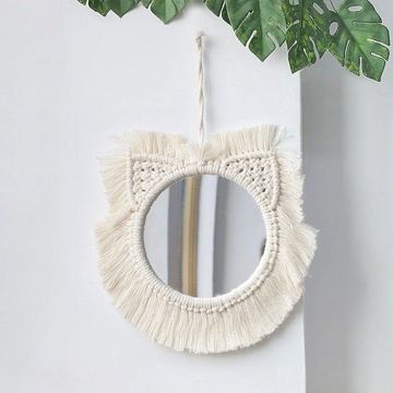 Round mirror with macrame fringe and cat ear design hanging on wall.