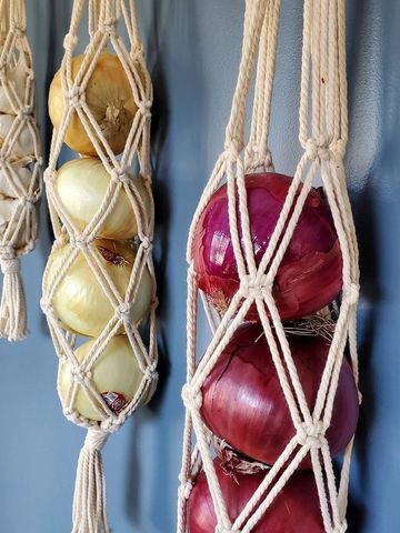 Onions hanging in macrame holders against a blue wall.