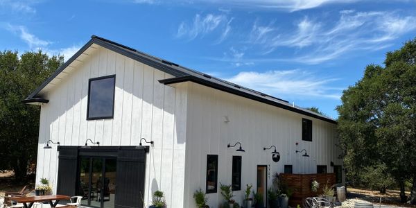 Modern white barn-style building under a blue sky with outdoor seating.