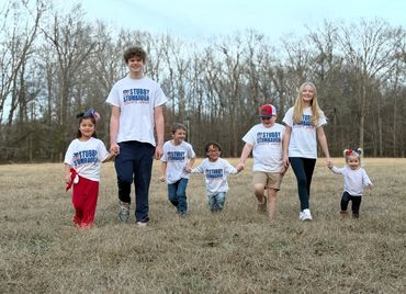 Seven children wearing matching campaign t-shirts, holding hands outdoors.