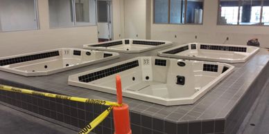 Four empty hot tubs on a tiled platform in an indoor setting.