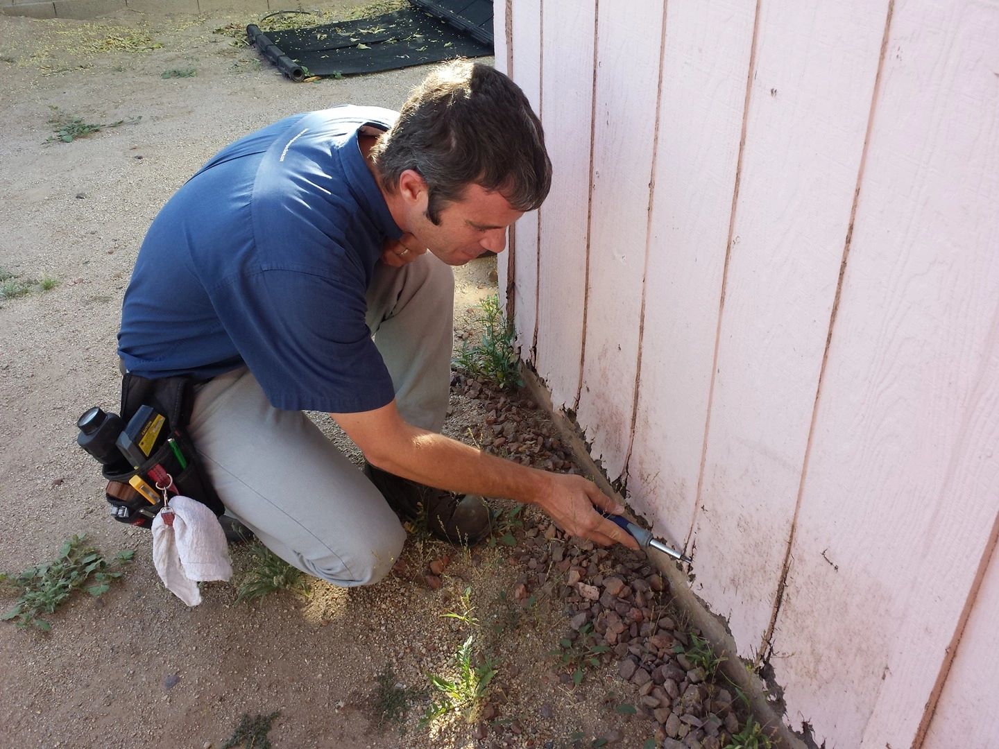 Man scraping damaged paint off a wooden wall outdoors.