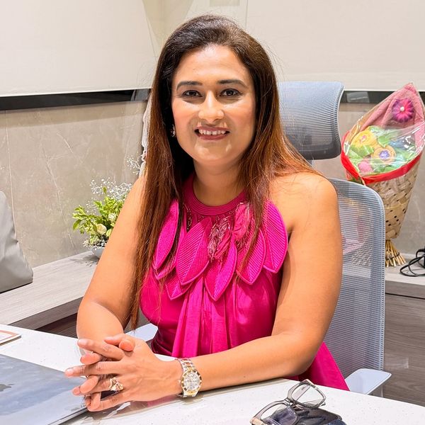 Woman smiling at desk in a bright pink dress.