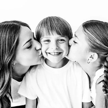 two sisters kissing their little brother on the cheeks. a black and white photo.
