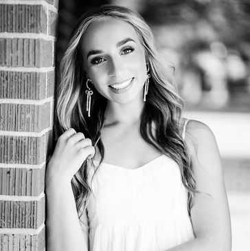 Black and white portrait of senior girl leaning on brick wall