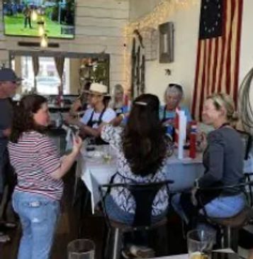 Group of people socializing around a table in a cozy room with an American flag on the wall.