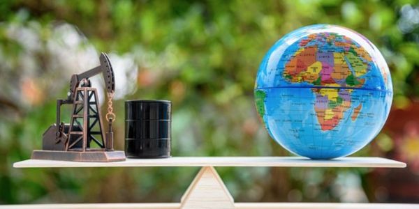 A balance scale with an oil pump and barrel on one side, and a globe on the other.