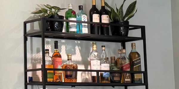 A black metal liquor shelf with bottles and potted plants mounted on a wall.