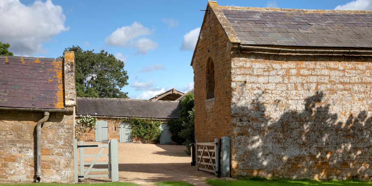 Sunny courtyard with rustic stone buildings and light blue gates.