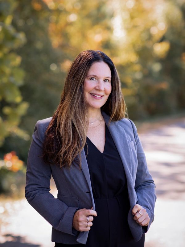Professional woman smiling outdoors in a blazer.