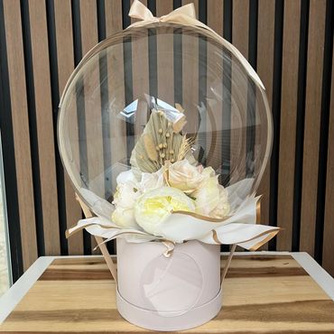 Neutral coloured box with ribbon and clear bubble balloon. Clear balloon has florals inside of it/