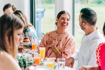 A joyful woman in a pink dress chatting at a luxury dining brunch gathering. Chef Joey private chef services at a local pop-up event by The Hidden Truffle.