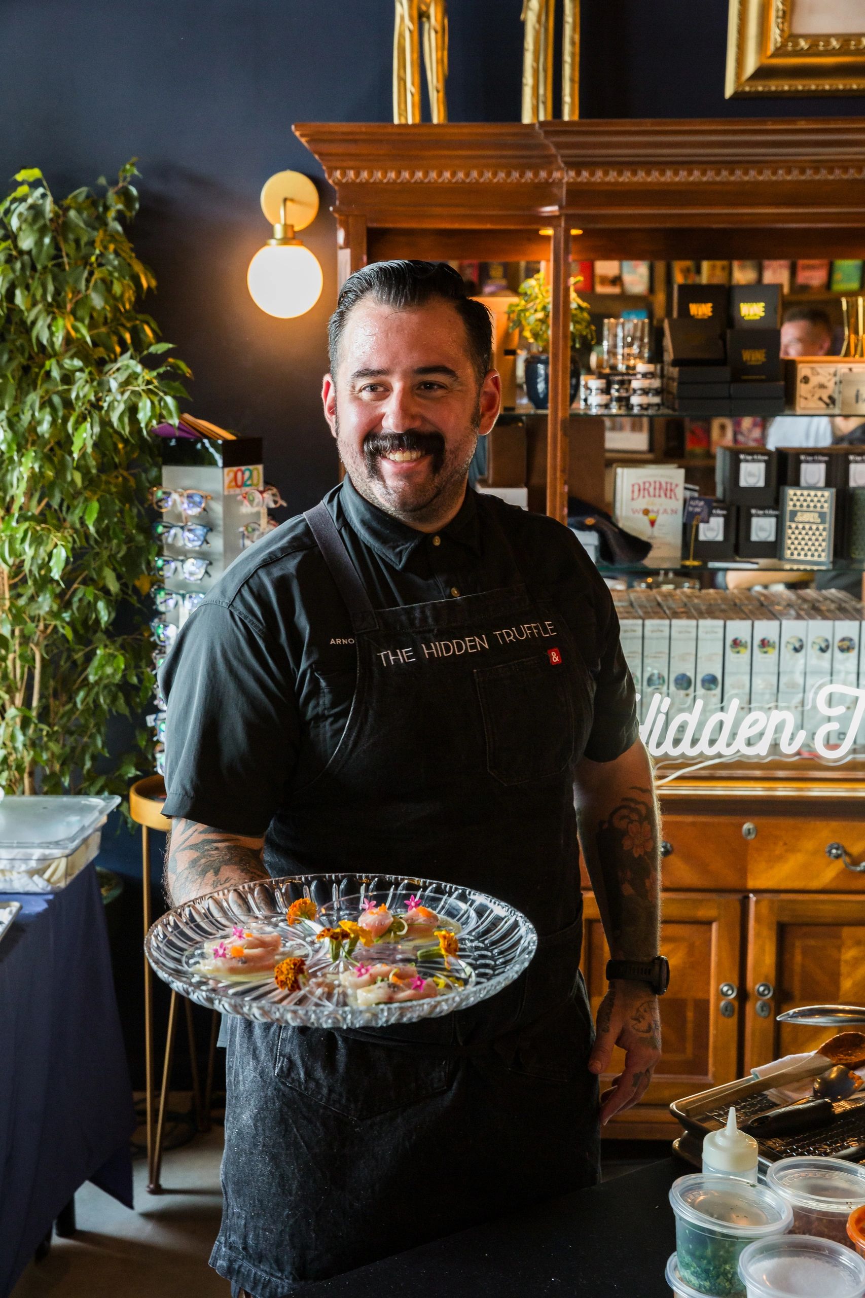 Chef Joey smiling while holding a plate of gourmet appetizers at LITbookbar. Private chef services for luxury dining local pop-up event