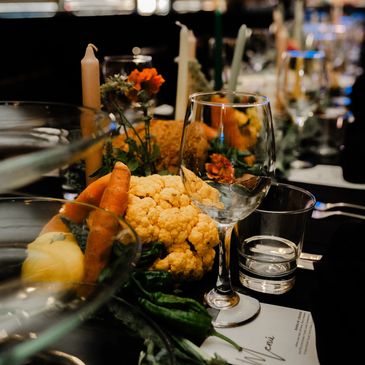 A beautifully set luxury dining table with vegetables, candles, and glassware in a cozy restaurant. Private chef services for local pop-up event by Chef Joey Chavez of The Hidden Truffle.