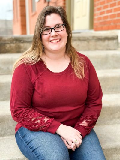 Woman in glasses smiling while sitting on outdoor steps.