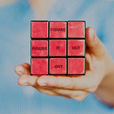 Hand holding a Rubik's cube with words 'FIGURE IT OUT' on red squares.