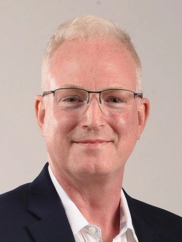 Smiling middle-aged man wearing glasses and a navy blazer.