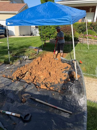 Person digging a hole under a blue canopy.
