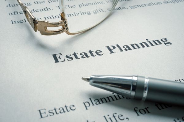 A close-up of "Estate Planning" text on a document, with a pen and glasses.