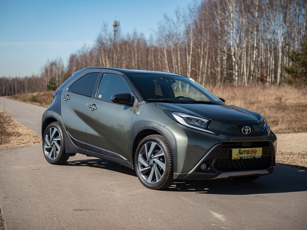 Toyota Aygo X STYLE grafit/czarny stoi prawym przednim bokiem na drodze asfaltowej obok traw