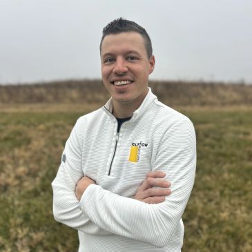 Man in white pullover standing outdoors with arms crossed.
