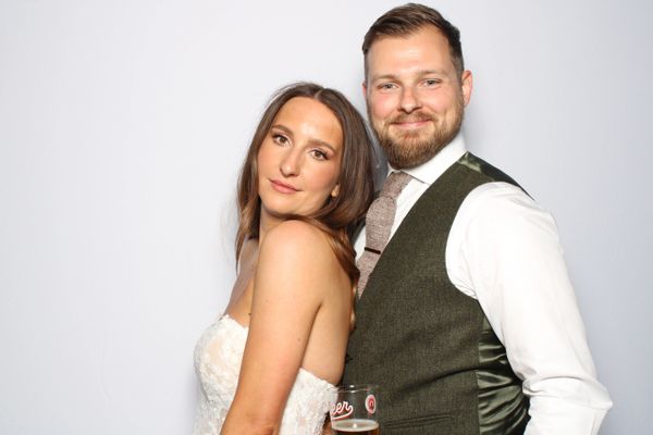 Bride and groom smiling for Photo Booth photo in front of white backdrop
