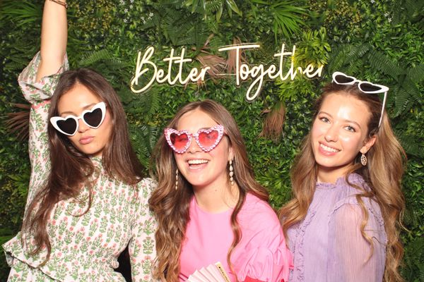 Three young women smiling for Photo Booth photo in front of botanical backdrop