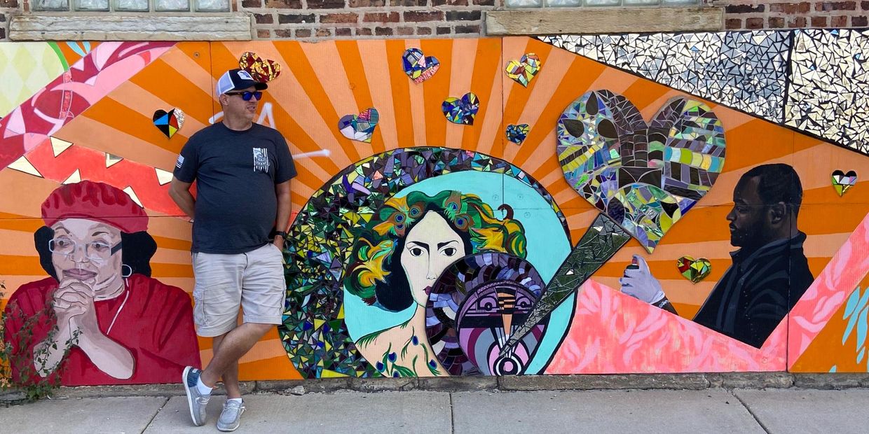 Man standing in front of colorful mural with mosaic hearts.