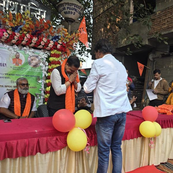 Man greeting another at an event decorated with balloons and flowers.