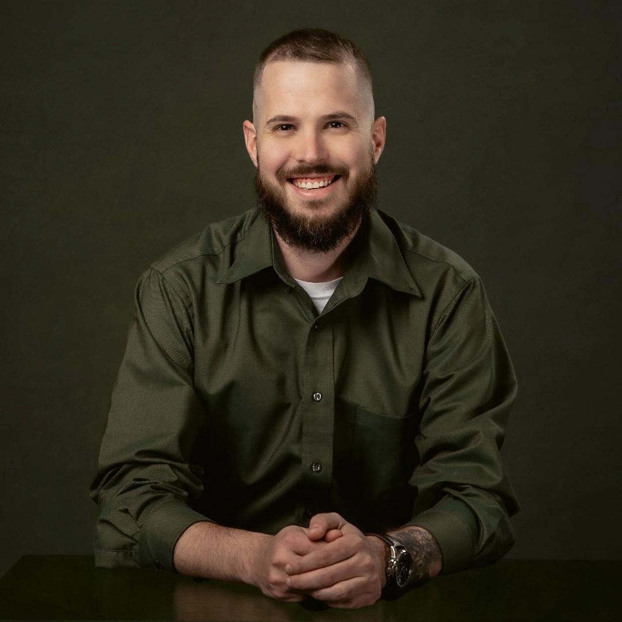 Smiling man with a beard in a green shirt sitting at a table.