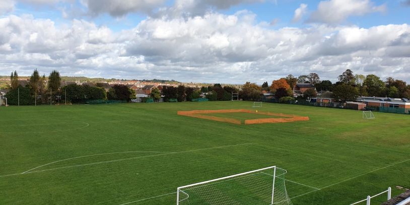 A sports field with soccer goals and a baseball diamond on a partly cloudy day.