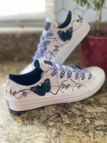White Converse with blue butterfly designs and checkered purple laces.