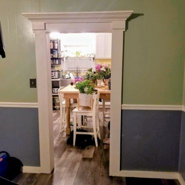 View through a doorway into a cozy kitchen with plants and flowers on a wooden table.