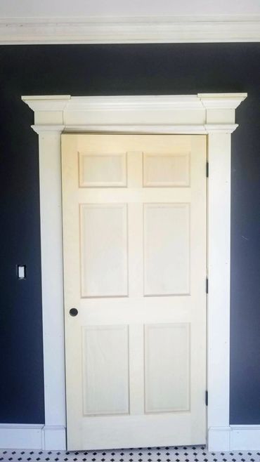 Classic white paneled door with decorative molding against a dark wall.