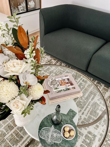 Modern lounge room with dark green lounge, brass & glass coffee table and textured rug