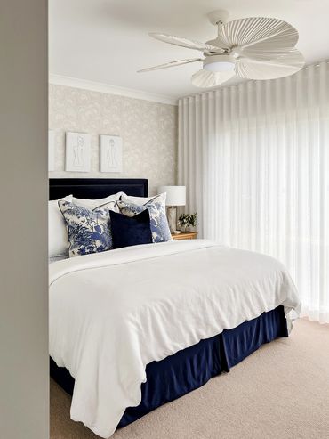 Light-filled Hamptons bedroom with linen curtains and bedding, wallpaper & navy velvet bedhead.