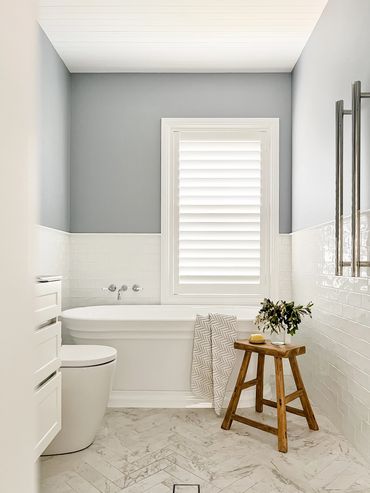 Light-filled Hamptons bathroom with herringbone marble floors, shaker cabinetry & soft blue feature