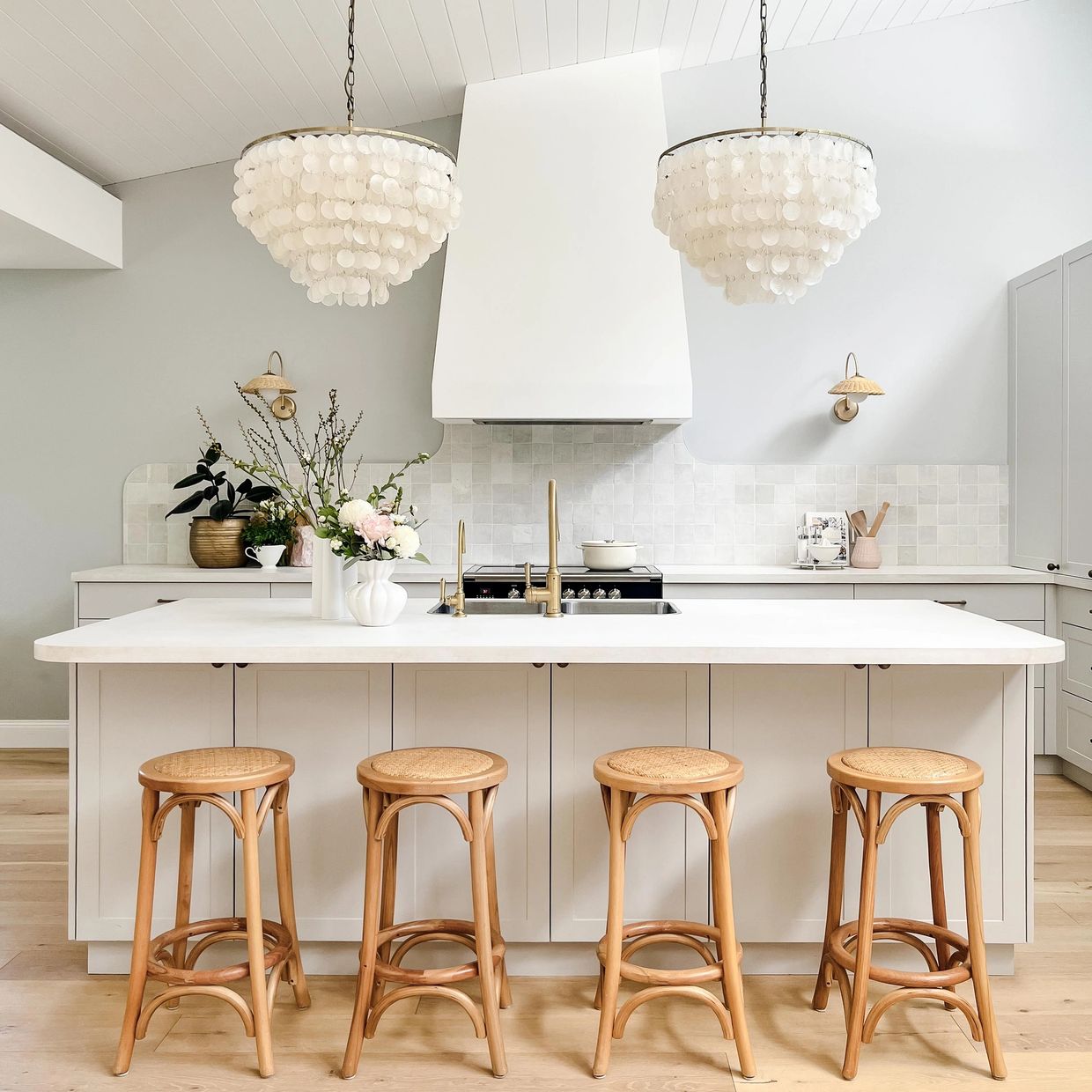 Light-filled coastal kitchen with shaker cabinetry, oak floors, zellige tiles and chandeliers.