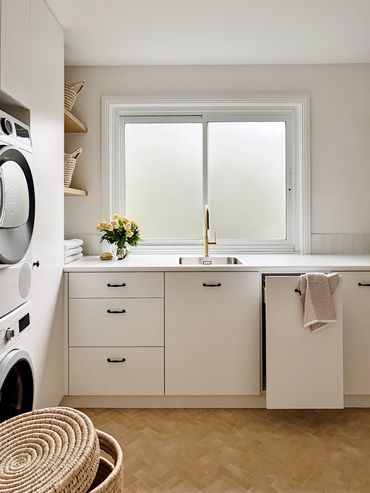 Light-filled, modern laundry with white cabinetry, herringbone floor tiles & floating timber shelf