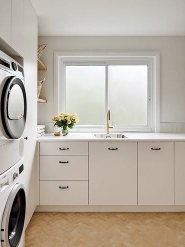 Light-filled, modern laundry with white cabinetry, herringbone floor tiles & floating timber shelf