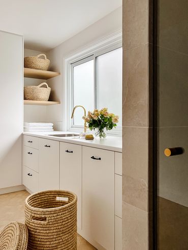 Light-filled, modern laundry with white cabinetry, herringbone floor tiles & floating timber shelf