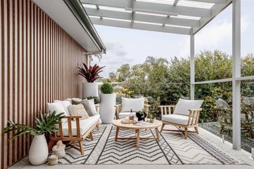 Outdoor lounge area with timber furniture, textured rug and timber feature wall.
