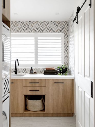 Mid-Century Modern Laundry with feature tile and oak cabinetry. Black tap and stone benchtop.