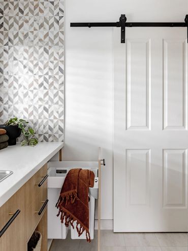 Mid-Century Modern Laundry with oak cabinetry. Black tap, stone benchtop & barn door.