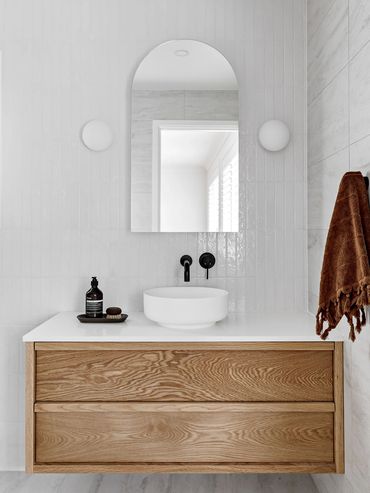 Modern light-filled bathroom with floating oak vanity, round wall lights and arch mirror.