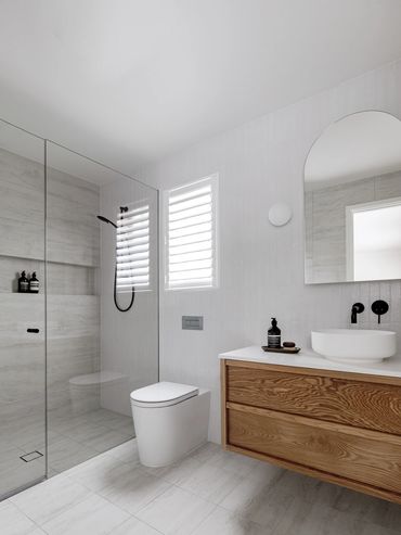 Modern light-filled bathroom with floating oak vanity, round wall lights and arch mirror.