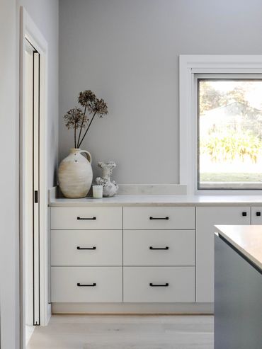 Light-filled white coastal kitchen with blue island, and oak flooring